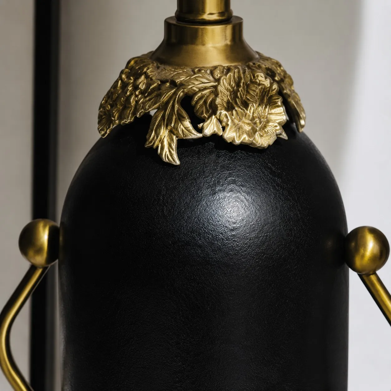 Close-up of matte black lamp body with antique brass-toned floral detail